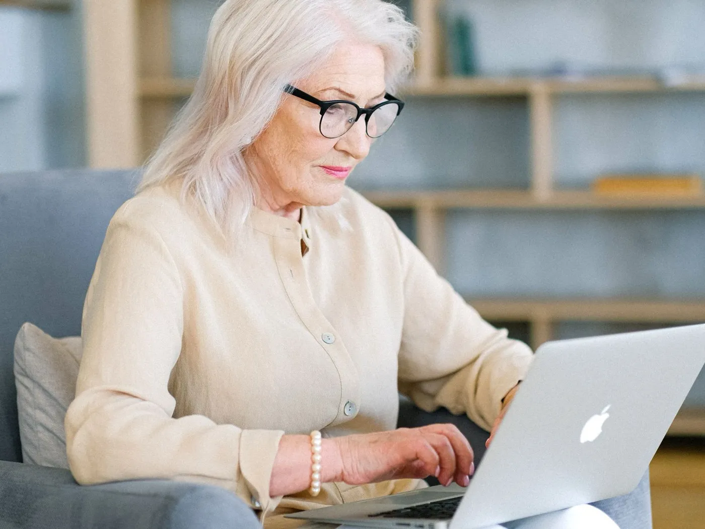 Een oudere vrouw zit aan tafel achter een laptop.