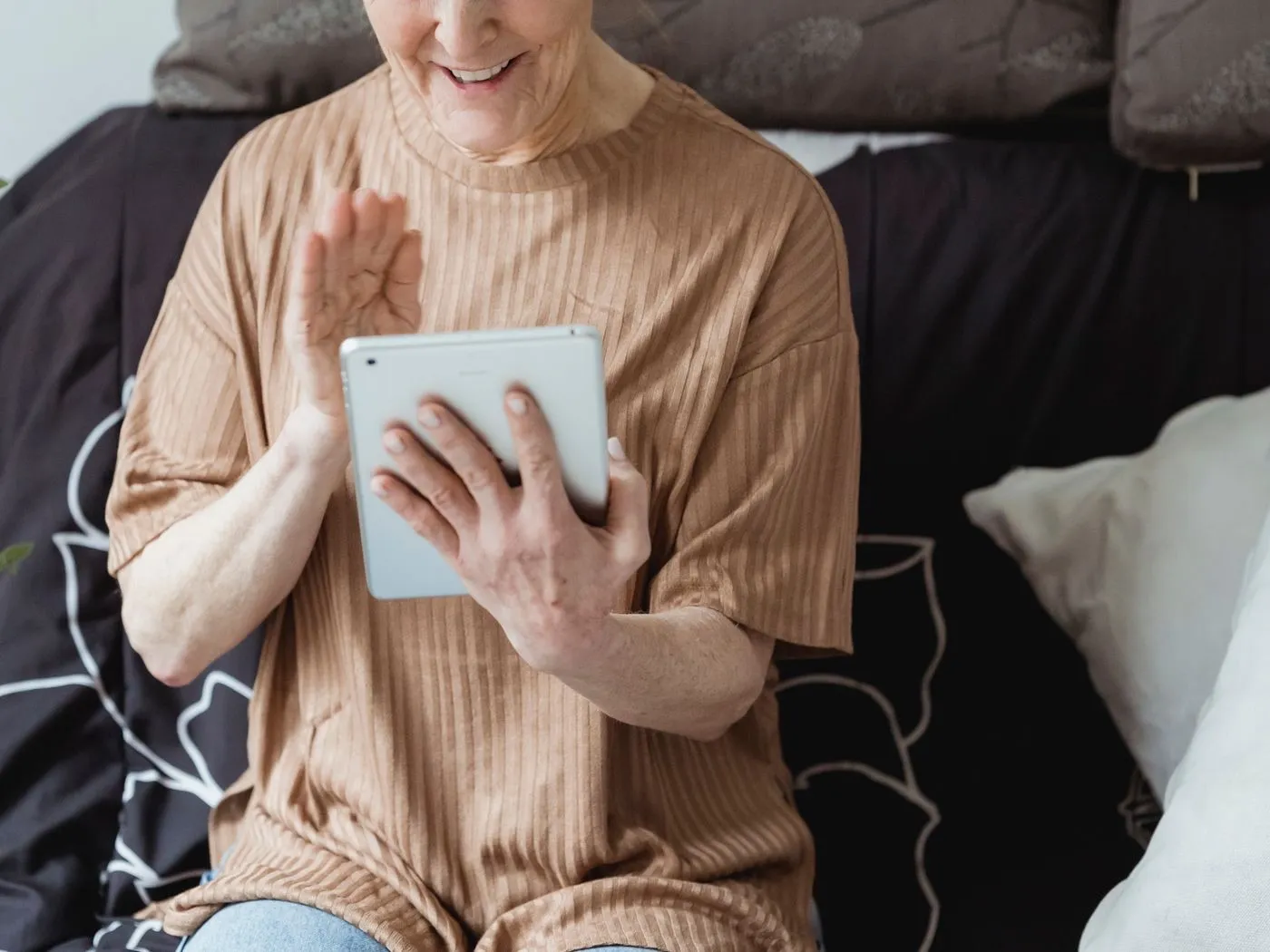 Een oudere vrouw houdt een tablet vast en zwaait naar het scherm.