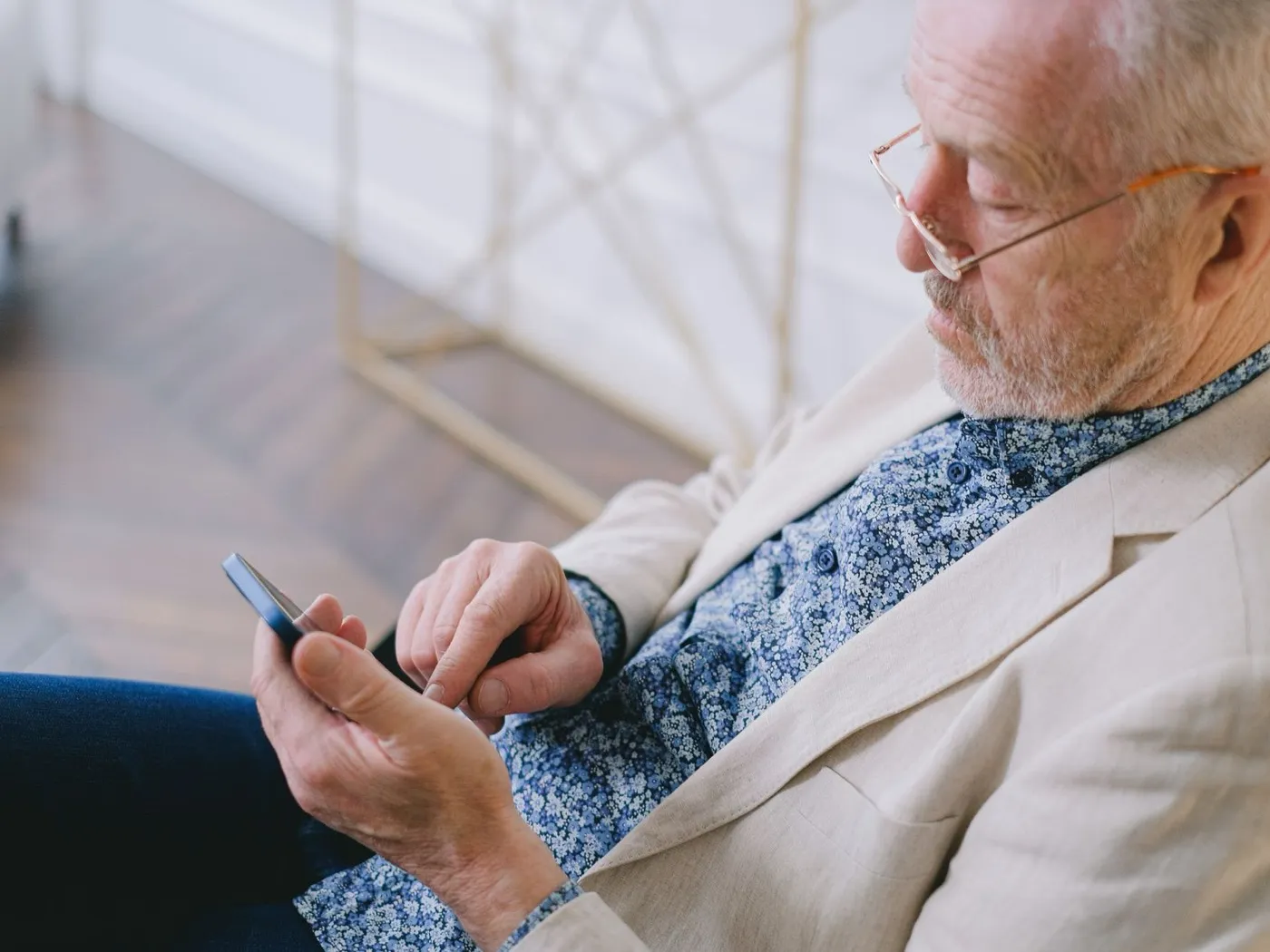 Een oudere man met een bril kijkt naar zijn mobiele telefoon.