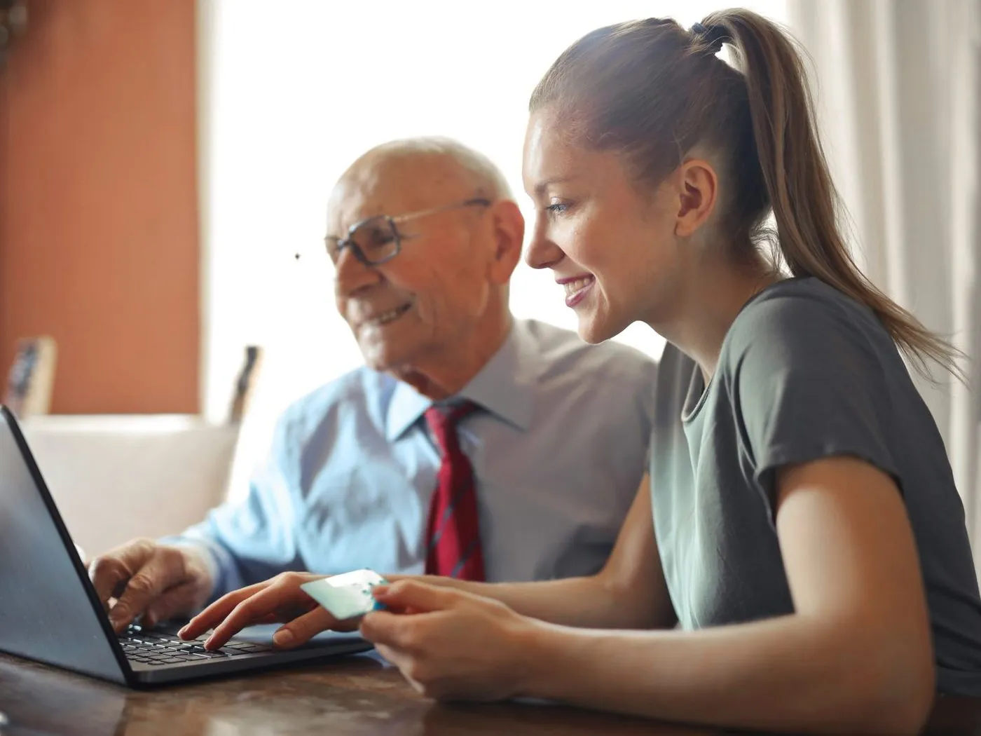 Een jongere vrouw en een oudere man kijken samen naar het scherm van een laptop aan de eettafel.