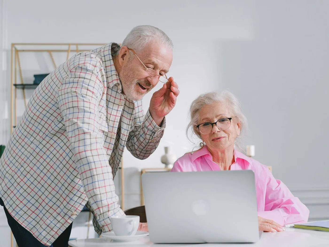 Een oudere man en een oudere vrouw kijken samen lachend naar een laptop.